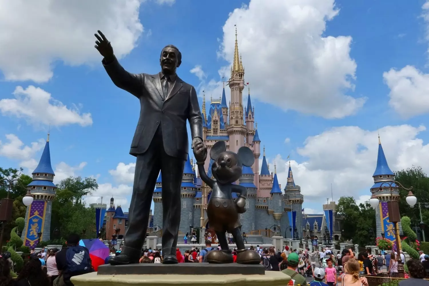 Iconic Magic: Mickey Mouse Statue with Cinderella Castle at Magic Kingdom Bronze statue of Mickey Mouse waving happily in front of the majestic Cinderella Castle at Disney World's Magic Kingdom, with colorful flowers and park guests in the background