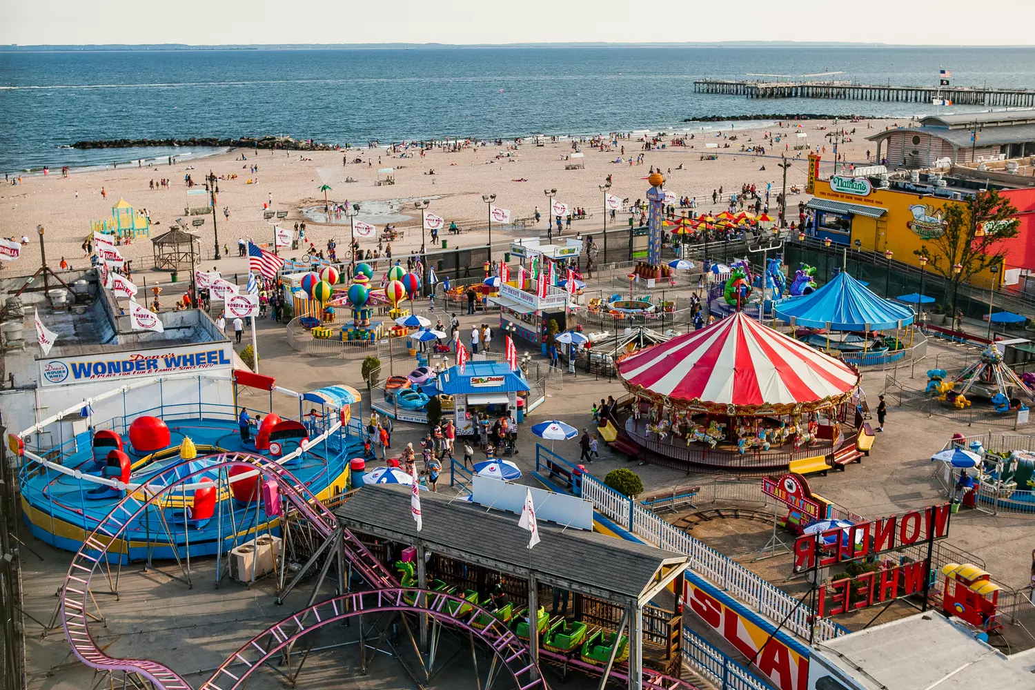 Coney Island Nostalgia: Where Americana Meets Ocean Breezes Iconic view of Coney Island's amusement park with the historic Cyclone roller coaster, Wonder Wheel, and vibrant boardwalk along the Atlantic Ocean shoreline