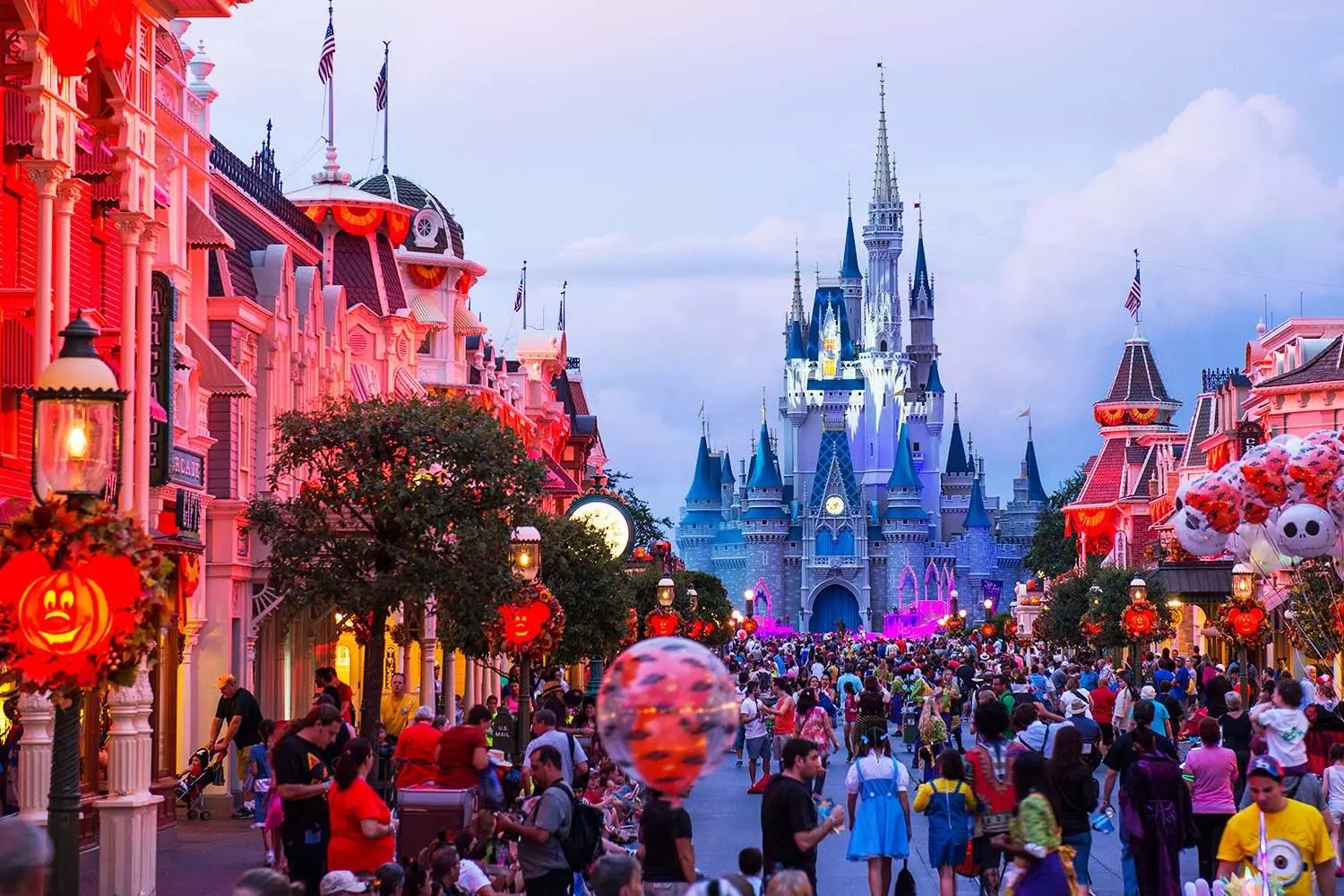 Spooktacular Disney Magic: Halloween Nights on Main Street, U.S.A. Decorated Halloween-themed Main Street at Disneyland with orange pumpkins, spooky garlands, and vintage lamps glowing under twilight, guests in costumes walking toward Cinderella Castle