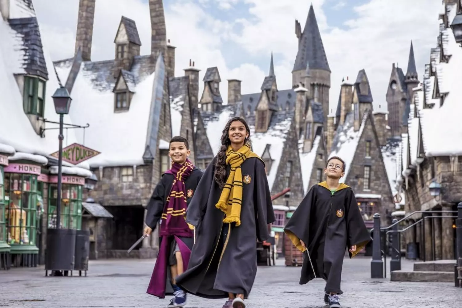 Step Into Magic: The Wizarding World of Harry Potter at Universal Orlando Hogsmeade village at The Wizarding World of Harry Potter with snow-capped roofs, the iconic Hogwarts Castle in the background, and visitors holding butterbeers near Honeydukes sweetshop