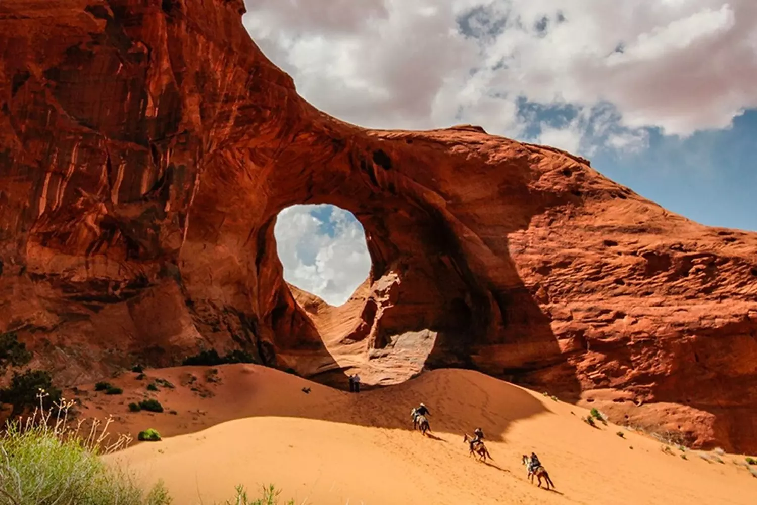 одлинный дух Дикого Запада: конная прогулка по Долине Монументов Группа всадников на лошадях исследует красные пески Долины Монументов на фоне величественных скал