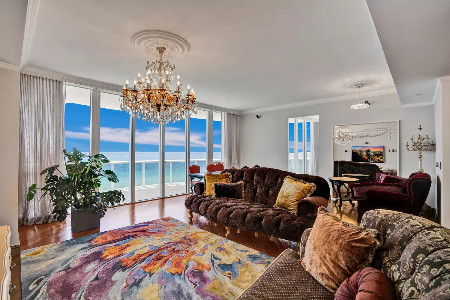 Гостиная квартиры Trump Towers II, unit 701 с диванами, хрустальной люстрой, большим зеркалом и телевизором Гостиная в Trump Towers II, unit 701 с мягкой мебелью, люстрой и видом на зеркало и телевизор